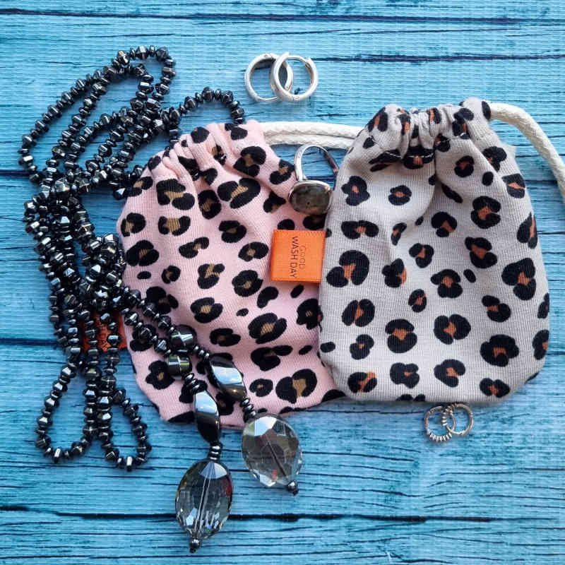 Three small drawstring bags: one black, one orange, and one with a leopard print pattern, each with a brown string and a small orange tag.