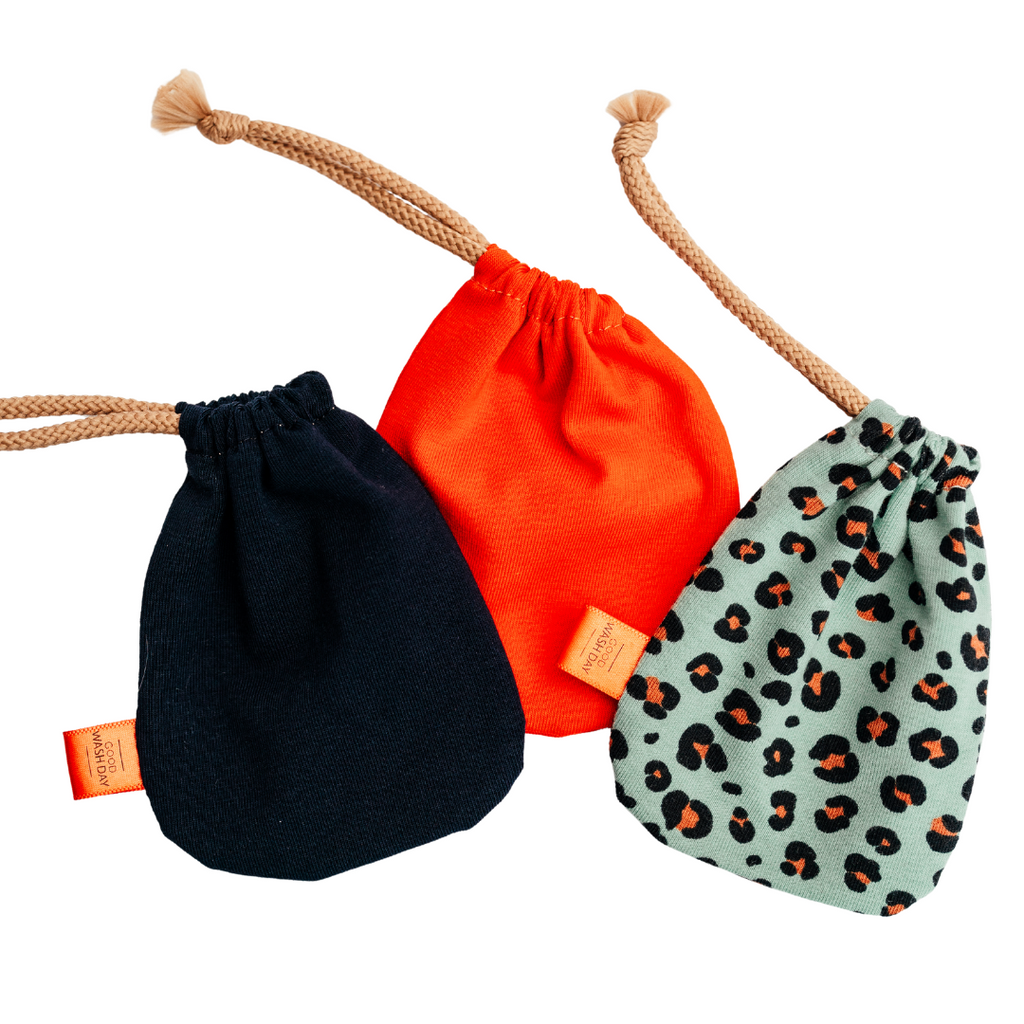 Five small drawstring bags from Good Wash Day, handmade in the UK from organic jersey fabric, in varying sizes and colors including red, black, and green leopard print, arranged in a scattered formation. Buy 2 Get 1 Free.