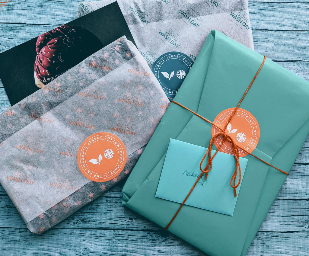 Three beautifully Wrapped Gift Wrap packages rest on a wooden surface, adorned with orange string. An envelope perched on top completes the order gift, adding a touch of anticipation.